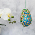 Load image into Gallery viewer, Golden Crown Easter Egg Beaded Ornament embellished with flowers, gold leaves, floral trim, and crystal beads. Side view. (Sky Blue).