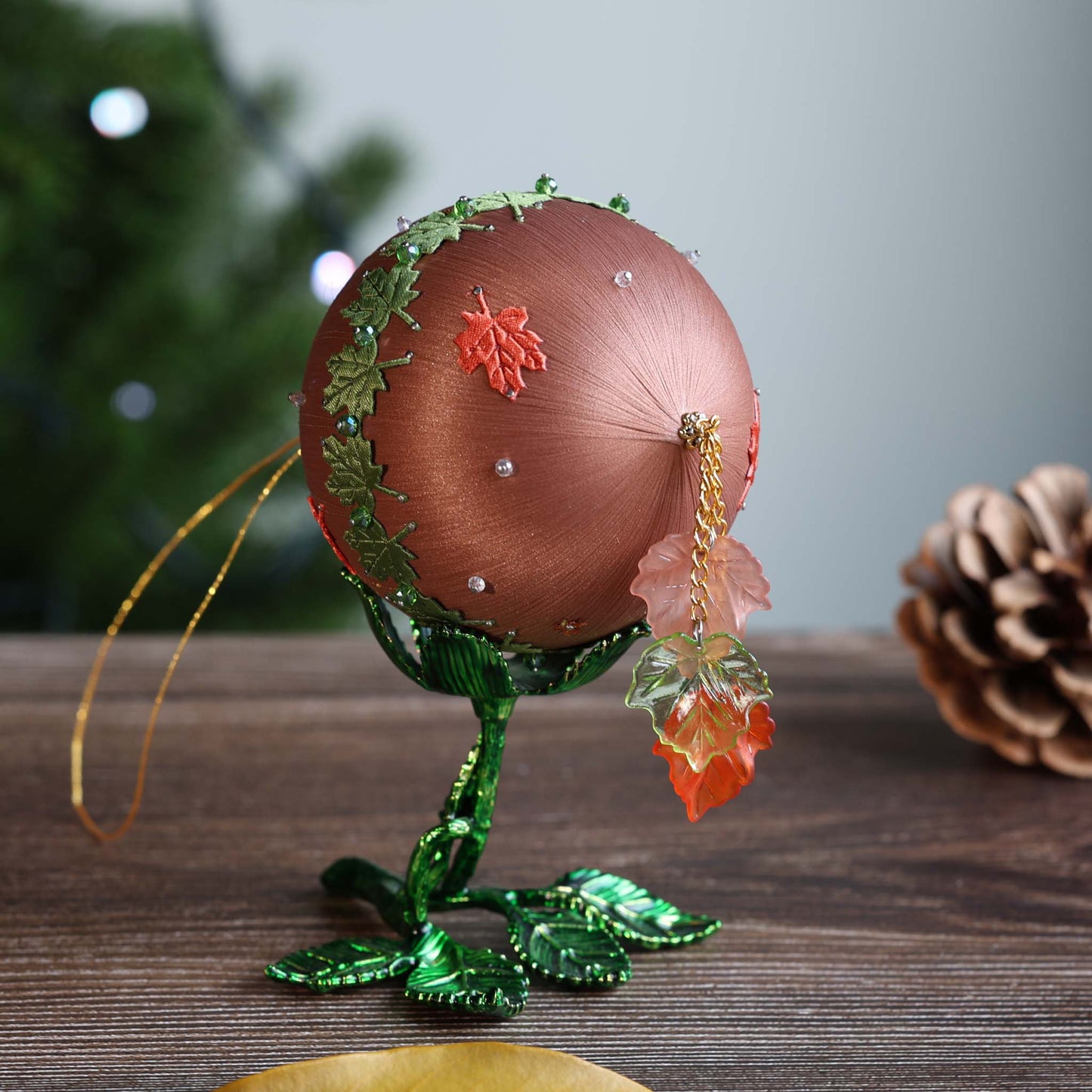 Close-up of the top of a beaded satin Christmas ornament with maple leaf tassel on a wooden surface. (RosyBrown)