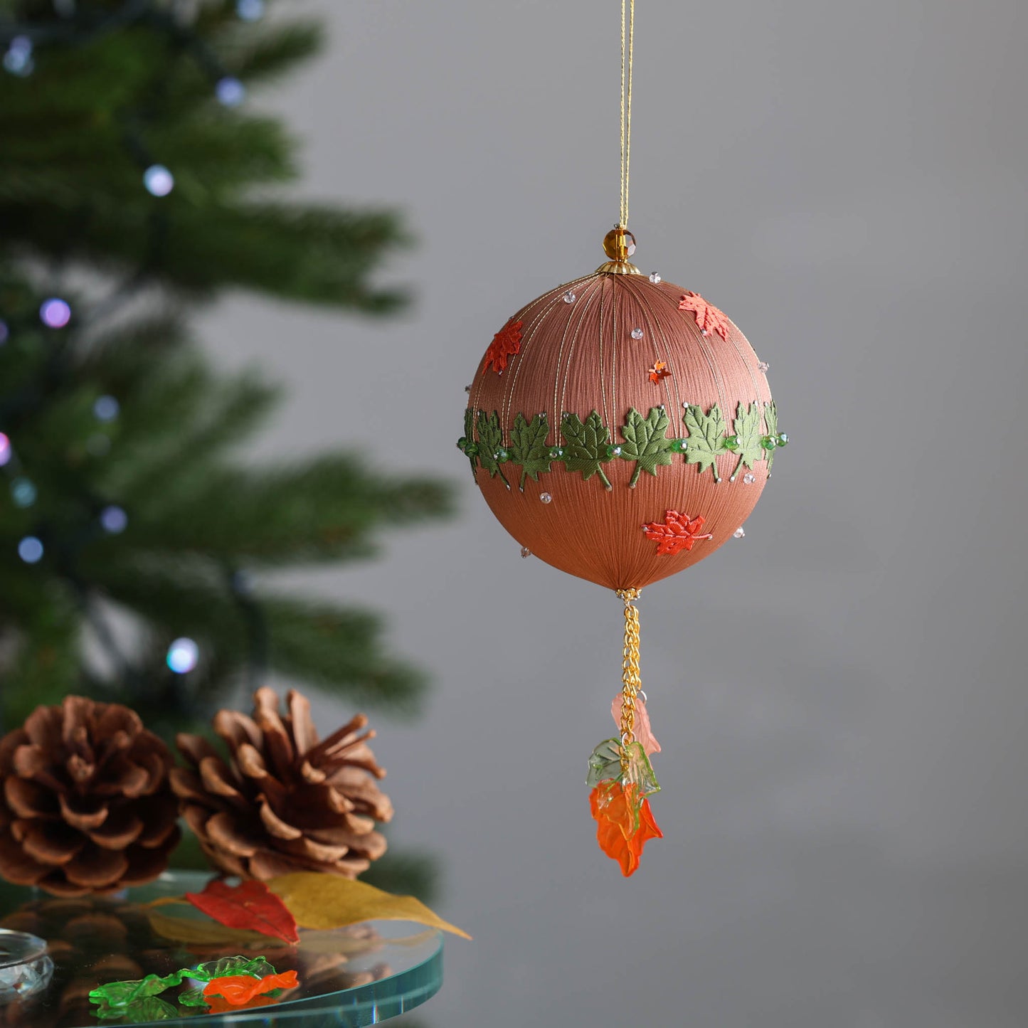 Finished Christmas ornament with green maple leaf details on a gray background with pinecones. (RosyBrown)