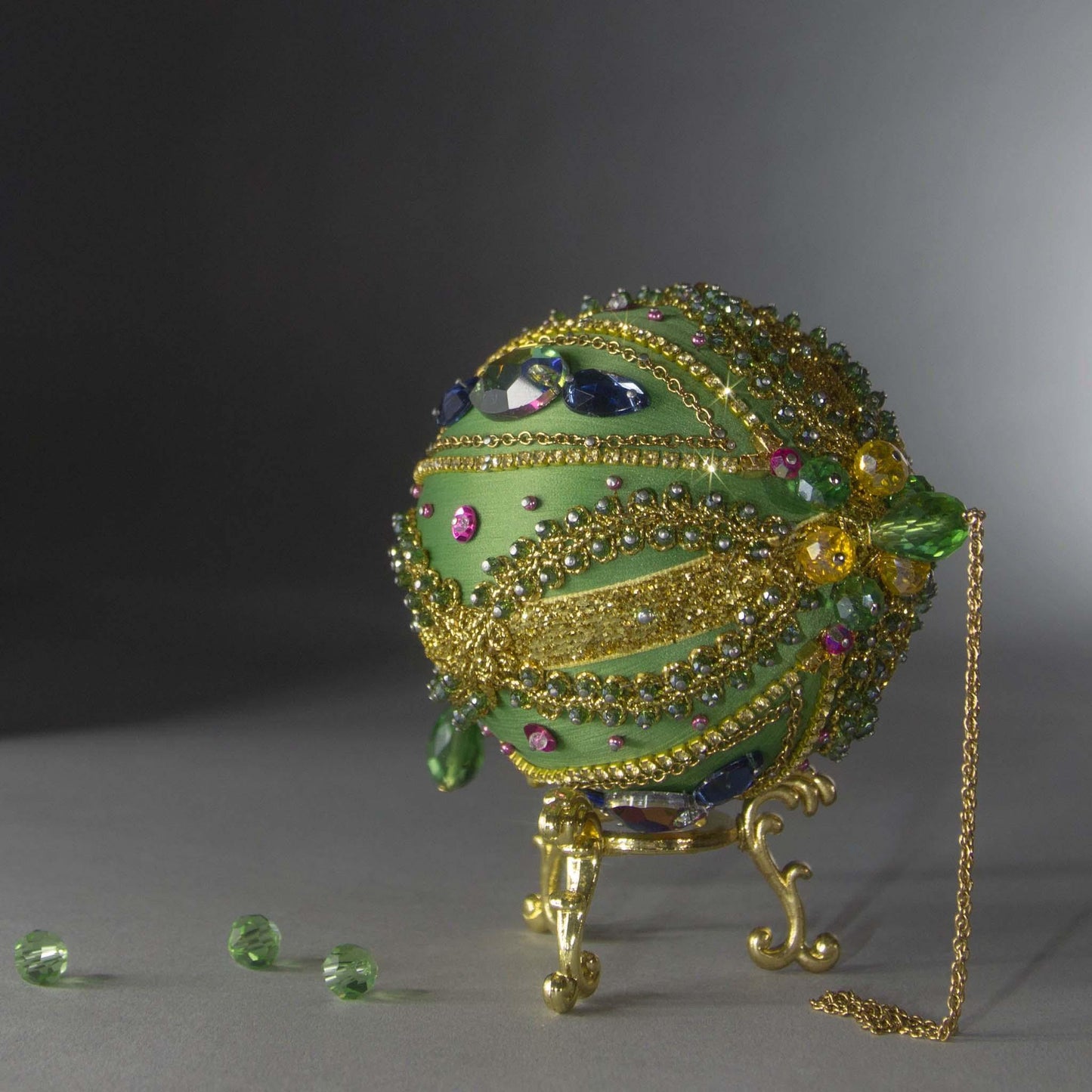 Christmas Beaded Ornament Ball embellished with large glass color-shifting rhinestones, gold braided trim, and crystal beads. Top detail. (Olive).