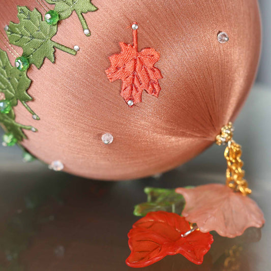A close-up of a Handmade Push Pin Ornament in rosy brown featuring a rust colored fabric maple leaf applique pinned to a satin foam core with dressmaker pins. (RosyBrown)