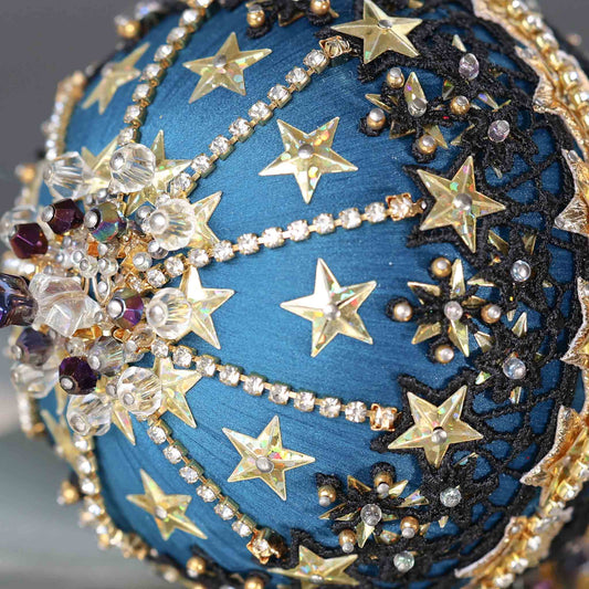 A close-up of dark purple beads and gold star-shaped sequins on a dark teal satin foam core ball featuring a completed handmade push pin ornament set against a dark gray background. (Dark Slate Blue)