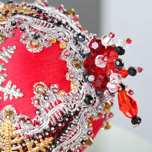 A close-up of a handmade push pin ornament's bottom with glass beads and metallic trim on a gray background. (Red)
