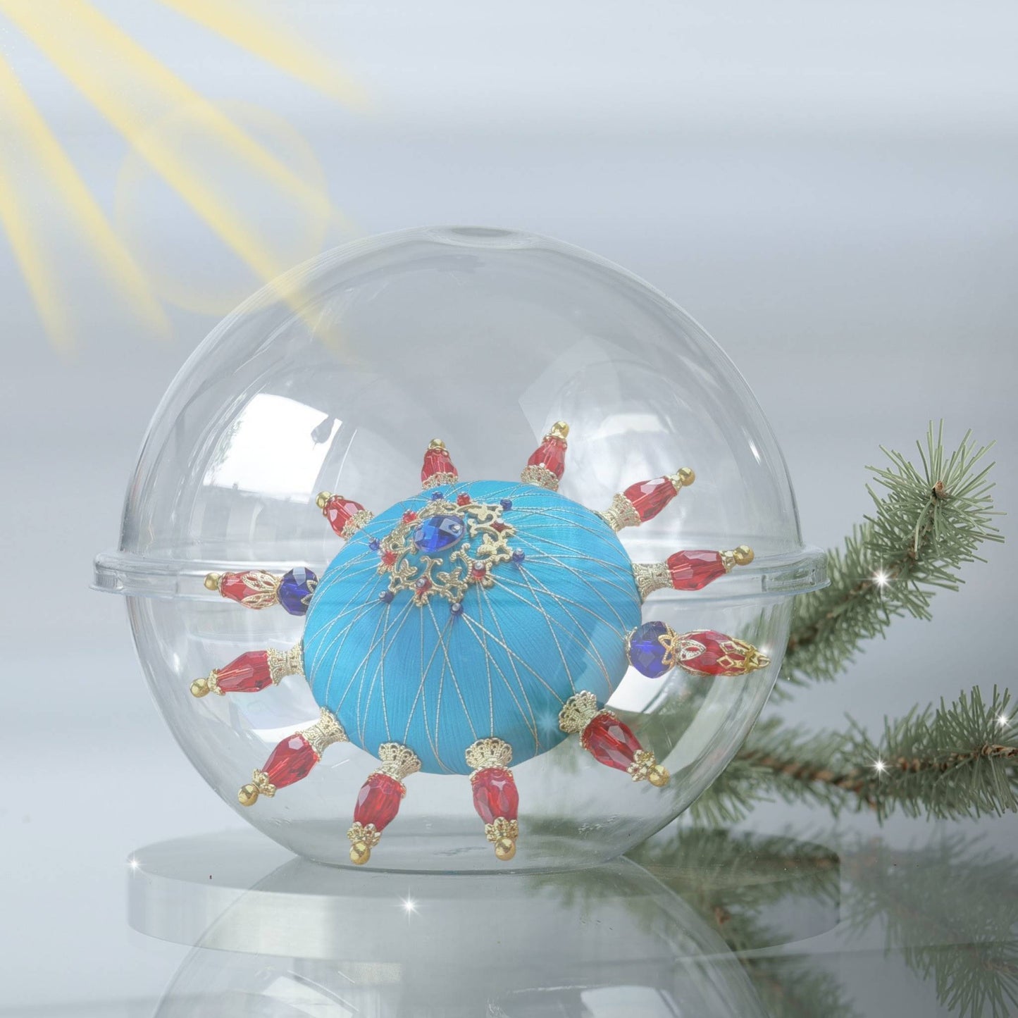 Christmas blue handmade ornament with red and gold accents inside a clear glass storage container, surrounded by pine branches and a pine cone by Whim5seasons.