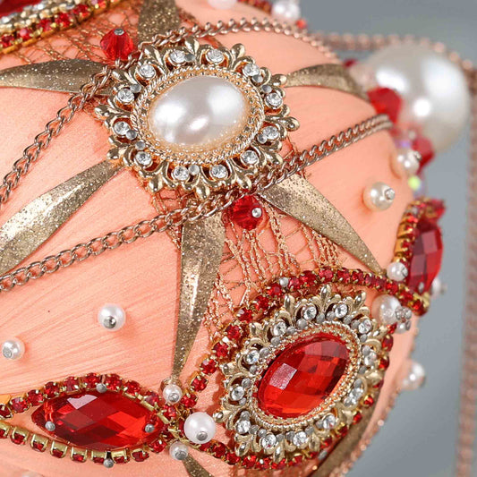 Close up of a handmade vintage style Christmas beaded ornament featuring large red rhinestones, gold trim, and pearl beads, pinned to a satin core with dressmaker pins by Whim5seasons. (Coral)