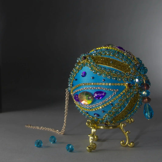 A close up of a bespoke handcrafted Christmas Beaded Ornament Ball, embellished with glass rhinestones, gold braided trim, and crystal beads attached to a satin foam core with dressmaker pins by Whim5seasons.