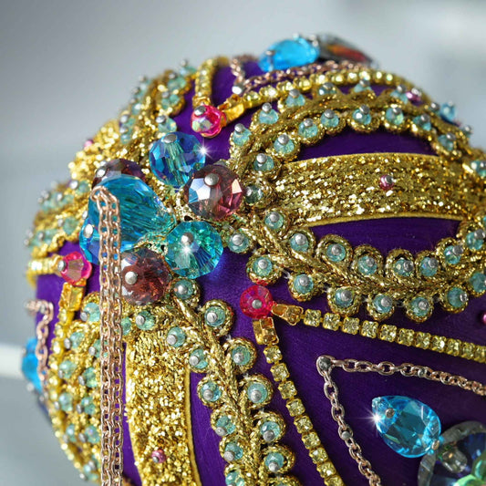 A close up of a bespoke handcrafted Christmas Beaded Ornament Ball, embellished with glass rhinestones, gold braided trim, and crystal beads attached to a satin foam core with dressmaker pins by Whim5seasons.