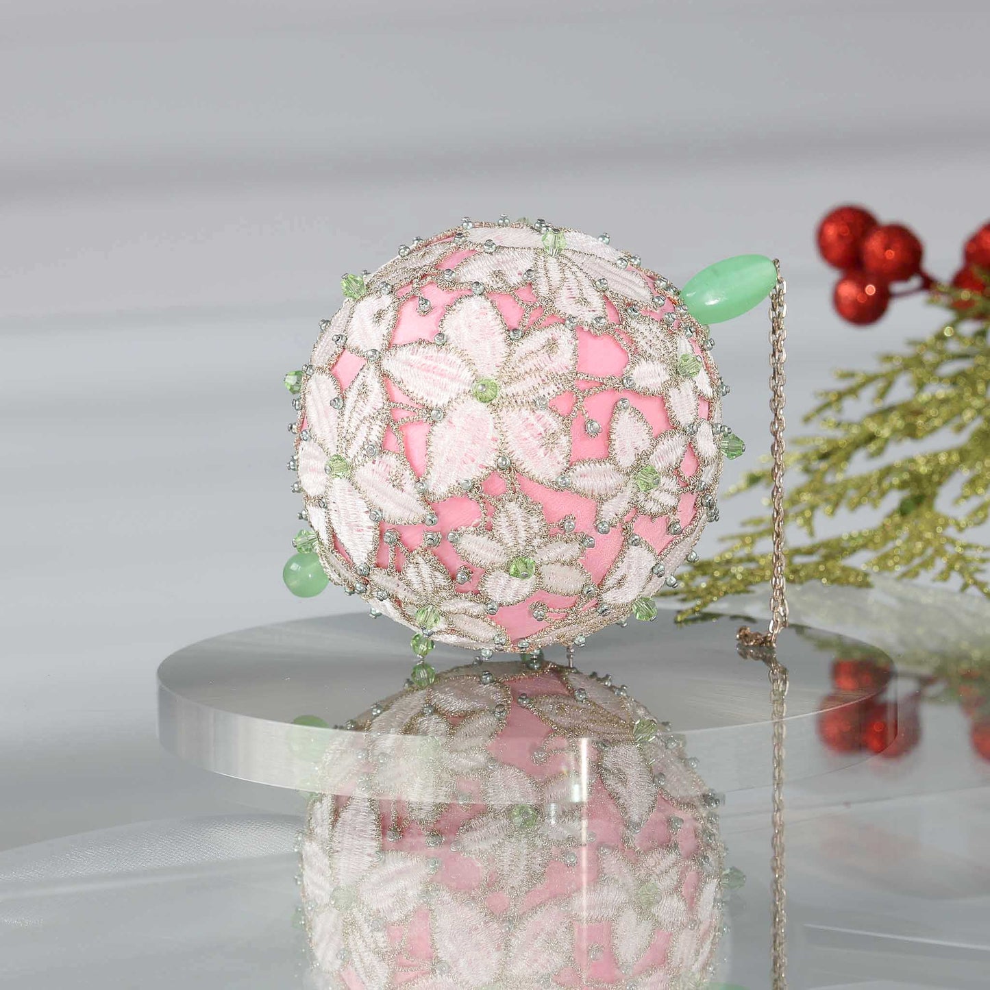 Handmade sequin & beaded pink satin ornament featuring flower trim with holiday greenery on a reflective surface by Whim5seasons.