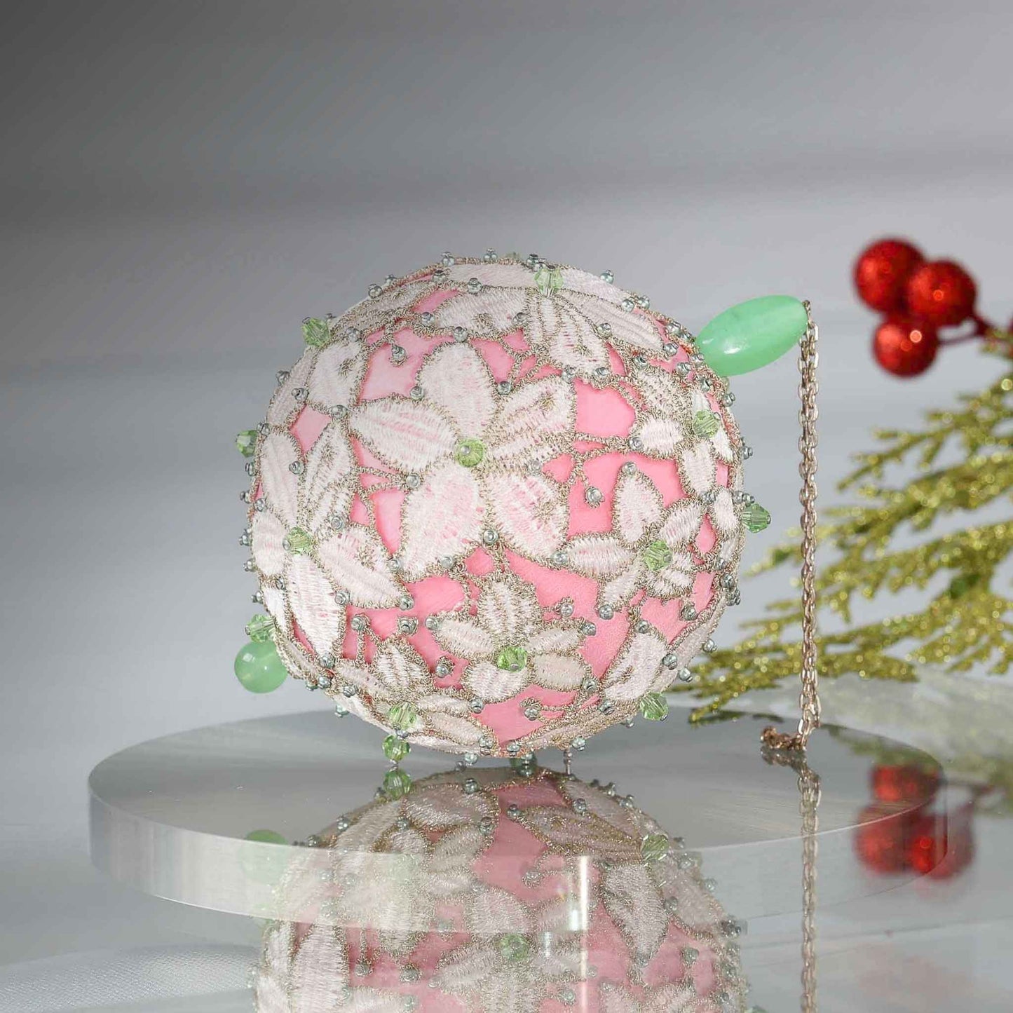 Handmade sequin & beaded pink satin ornament featuring flower trim with holiday greenery on a reflective surface by Whim5seasons.
