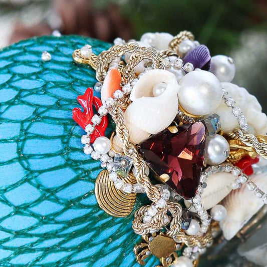 Handmade sequin & beaded blue satin ornament featuring large glass rhinestone, pearls, crab, and anchor charms on a reflective surface by Whim5seasons.