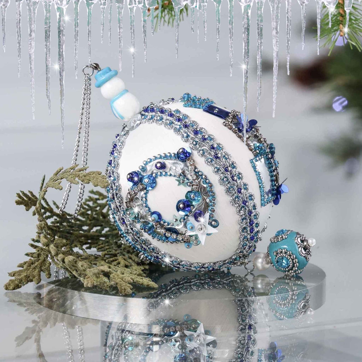 Handmade Christmas satin push pin ornament in white with blue and silver sequined holiday wreath, snowman bead, and a large Tibetan style bead with green branches on a gray background by Whim5seasons.