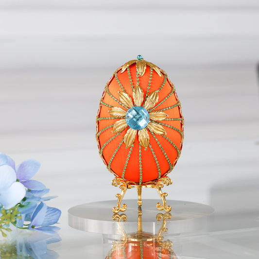 A handmade large Easter egg push pin ornament with a large gold flower on a gold stand on a reflective surface.