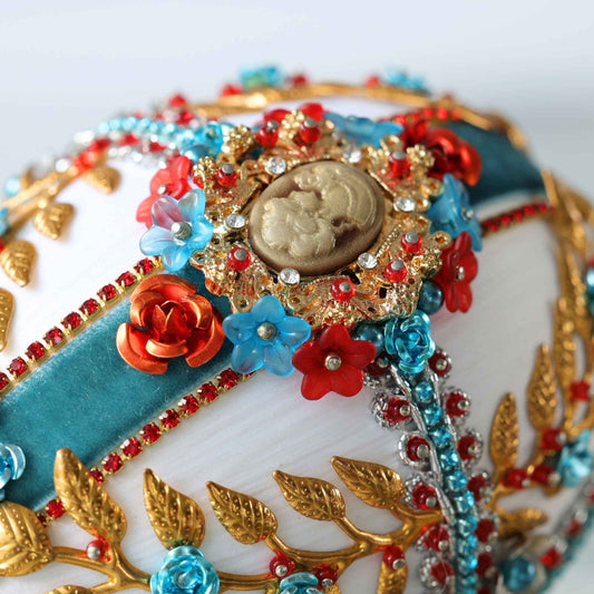 A close up detail of a handmade sequin & beaded satin ornament showing how a large gold cameo is attached to a satin foam core with dress maker pins by Whim5seasons.