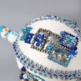 Load image into Gallery viewer, Close up of white handmade Christmas beaded push pin ornament in with sequined blue gift boxes and a snowman porcelain bead in the background.