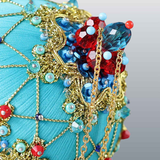 Close-up detail of a handmade push pin ornament - satin foam ball with red rhinestones, blue accents, sequins, seed beads, gold chain, and a metallic cord. (Light Sea Green)