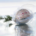 Load image into Gallery viewer, Handmade Christmas beaded ornament with intricate design on a reflective surface in a clear storage box with an evergreen branch in the background.