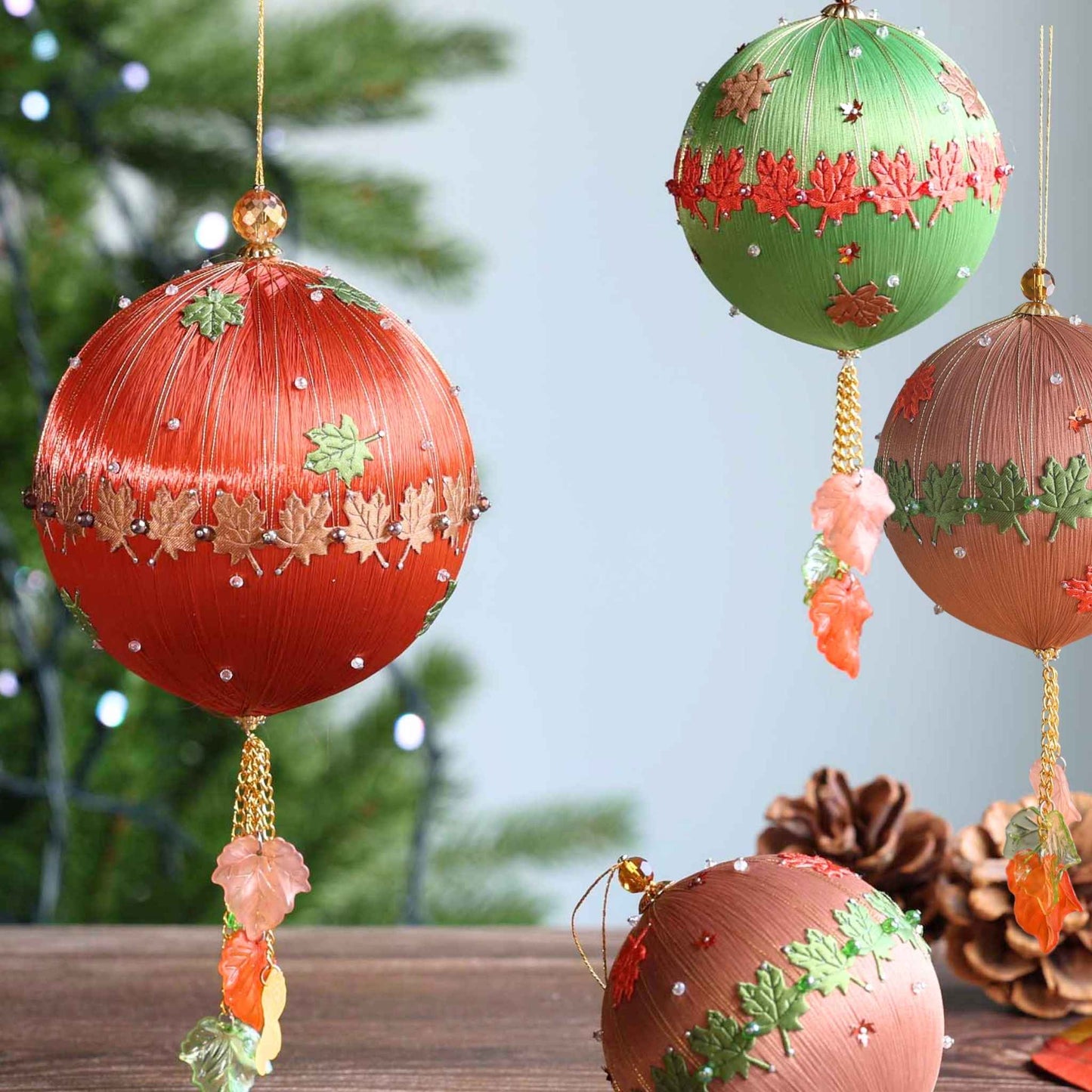 Collection of three completed handmade push pin ornaments in green, brown, and rust color in front of a Christmas tree on a wooden tables with some pinecones by Whim5seasons.