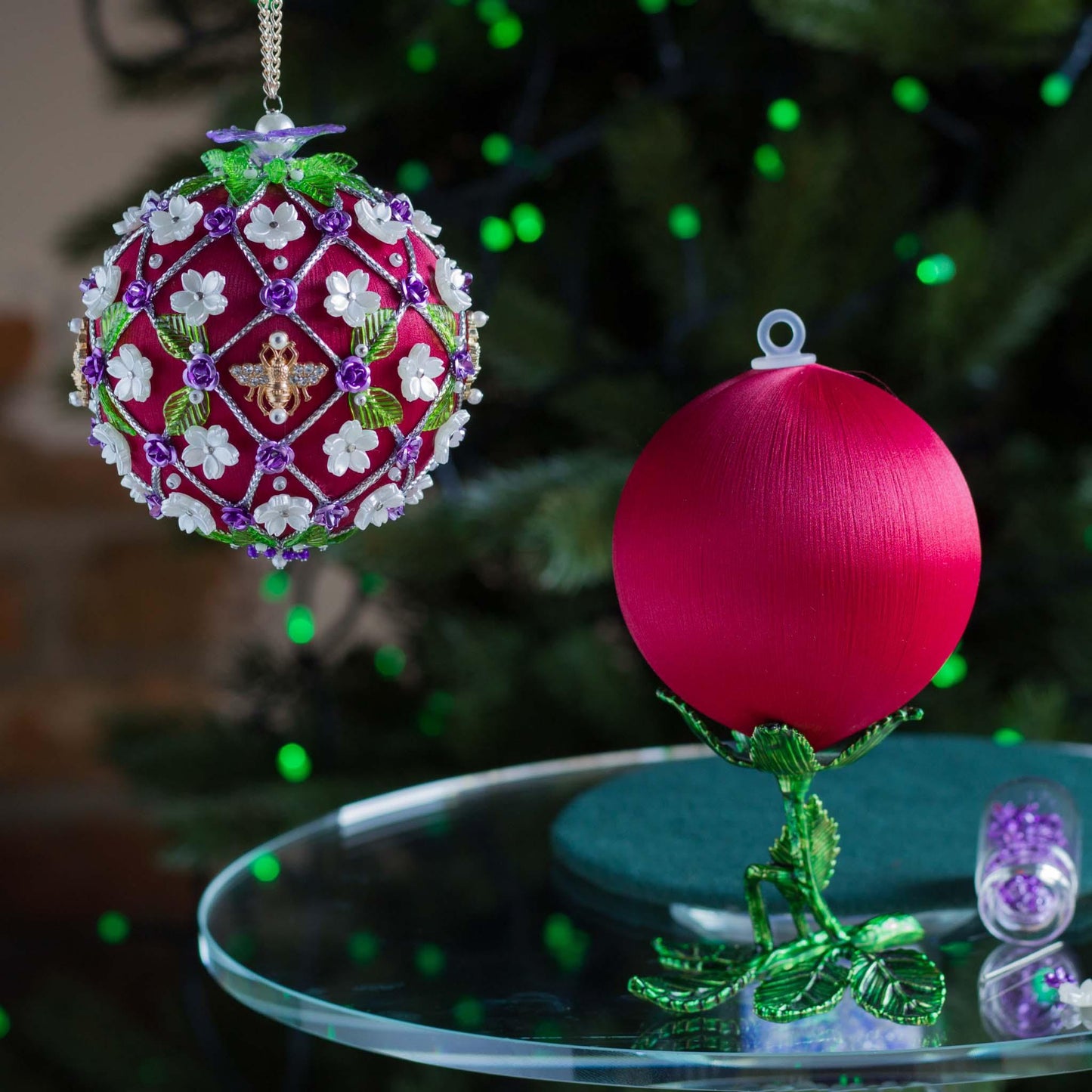 Decorative Christmas ornament with intricate design on a table in front of a blurred Christmas tree. (Dark Red).