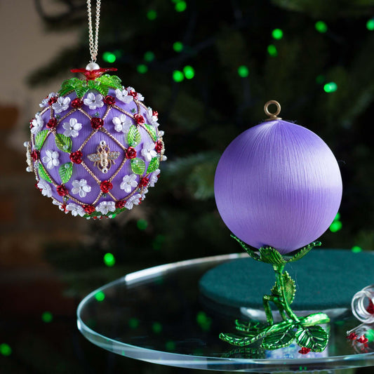Decorative Christmas ornament with intricate design on a table in front of a blurred Christmas tree. (Medium Purple).
