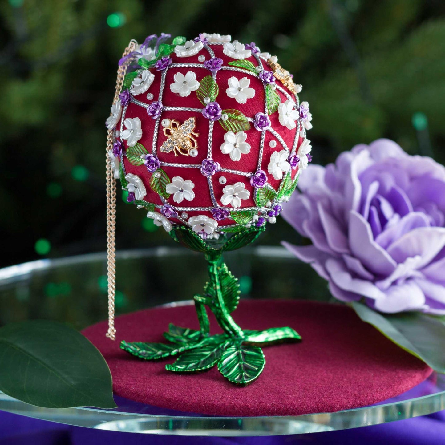 Push Pin Satin Ornament with floral pattern on a stand, surrounded by flowers and leaves. (Dark Red).