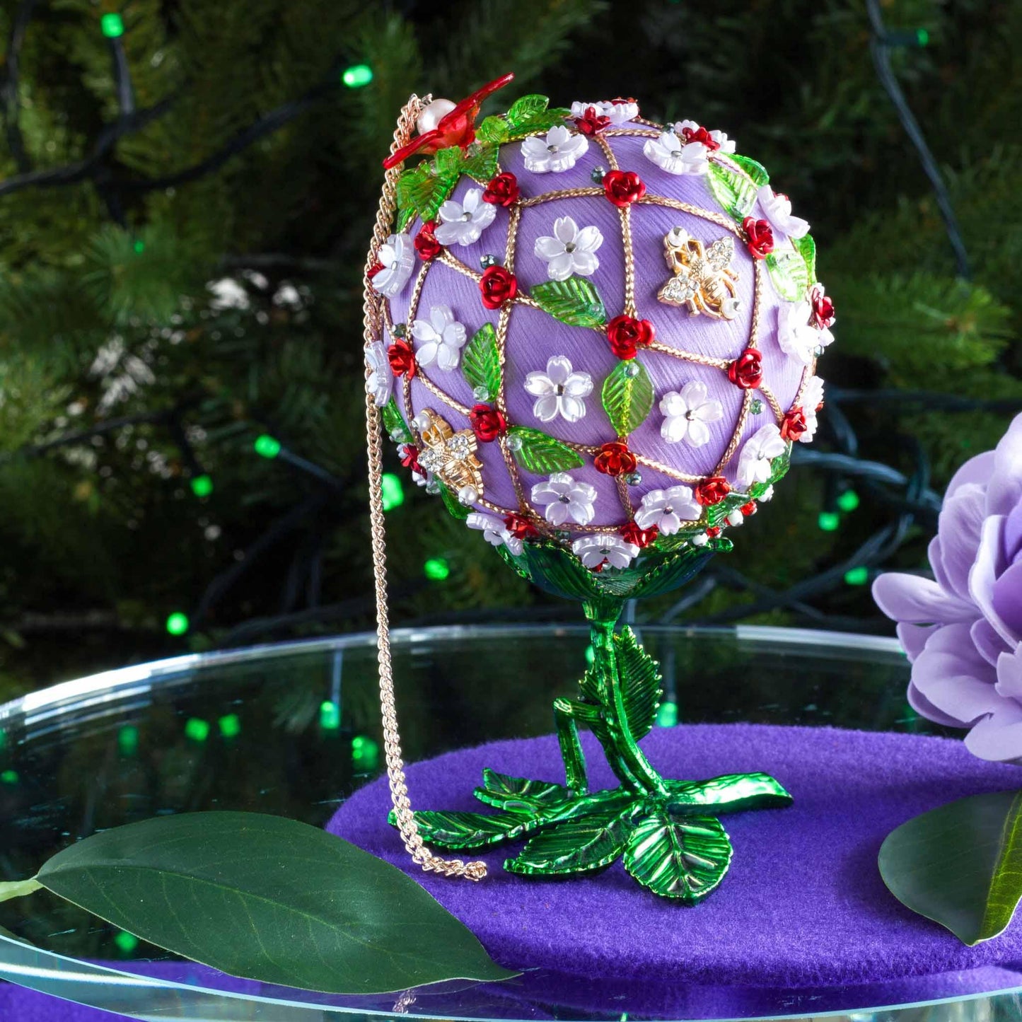 One-of-a-kind handmade Floral ornament on a green metal stand against a greenery background. (Medium Purple).