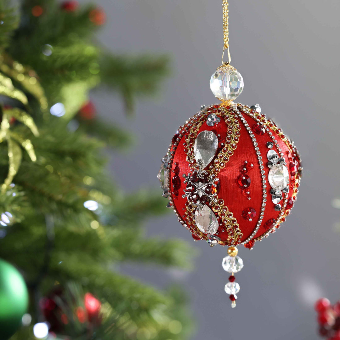 Large sparkly red Christmas satin ornament with beads and crystals on a blurred Christmas tree background