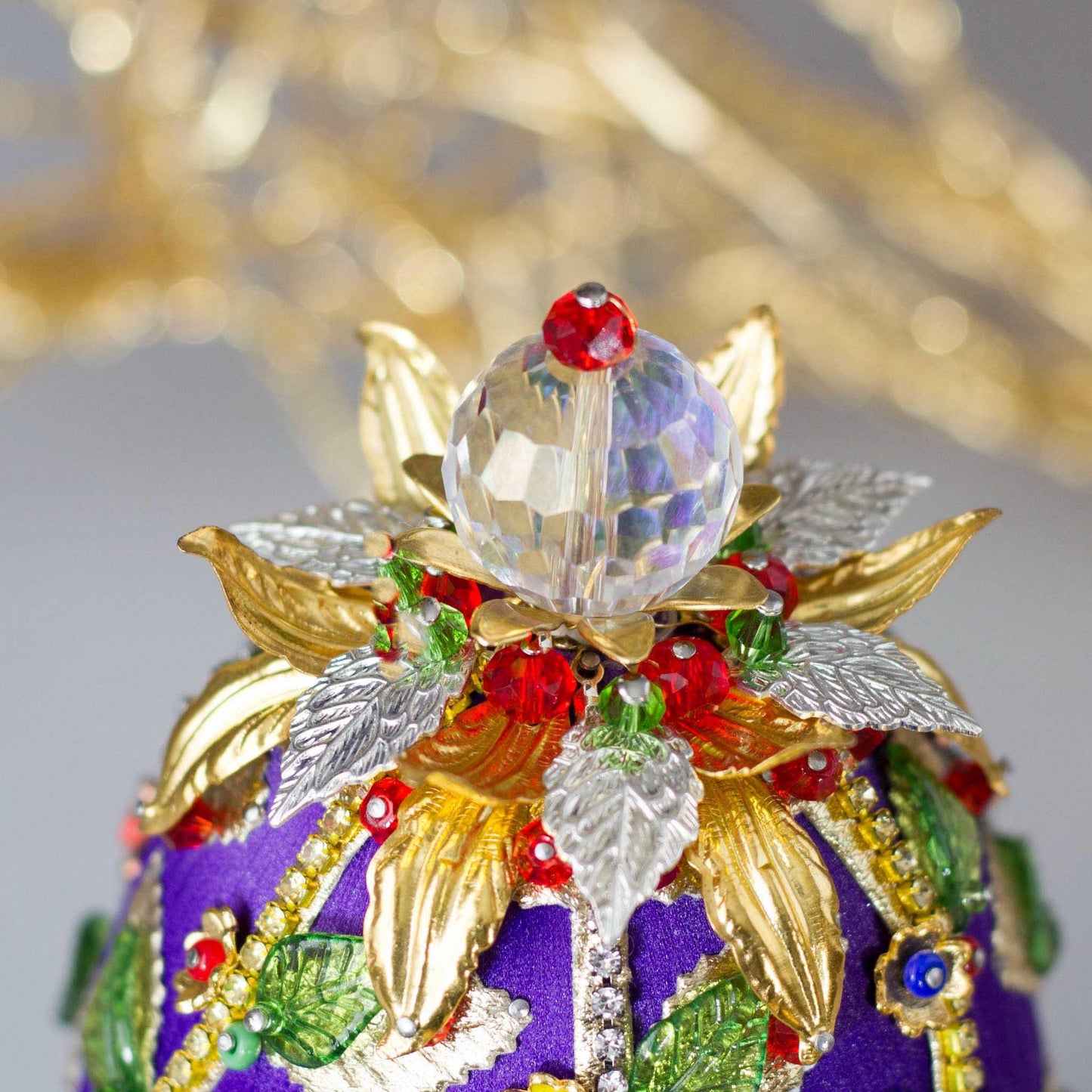 Easter Egg Handmade Ornament embellished with flowers, leaves, gold floral trim, and crystal beads - close-up of a top crystal beadl. (Indigo).