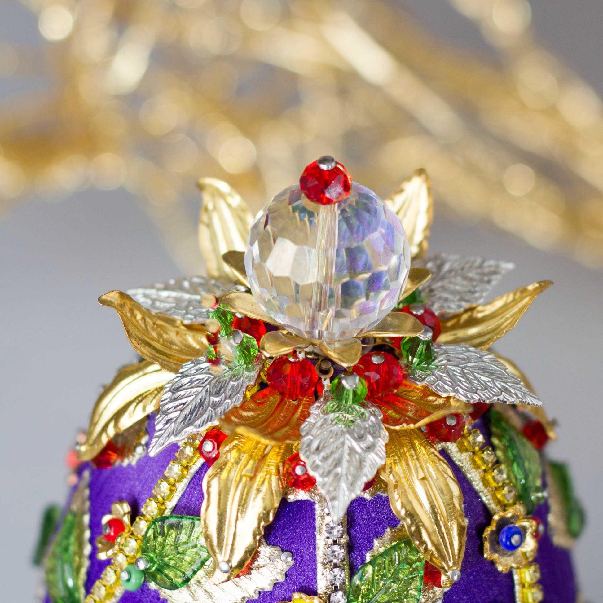 Easter Egg Handmade Ornament embellished with flowers, leaves, gold floral trim, and crystal beads - close-up of a top crystal beadl. (Indigo).