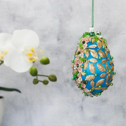 Golden Crown Easter Egg Beaded Ornament embellished with flowers, gold leaves, floral trim, and crystal beads. Side view. (Sky Blue).