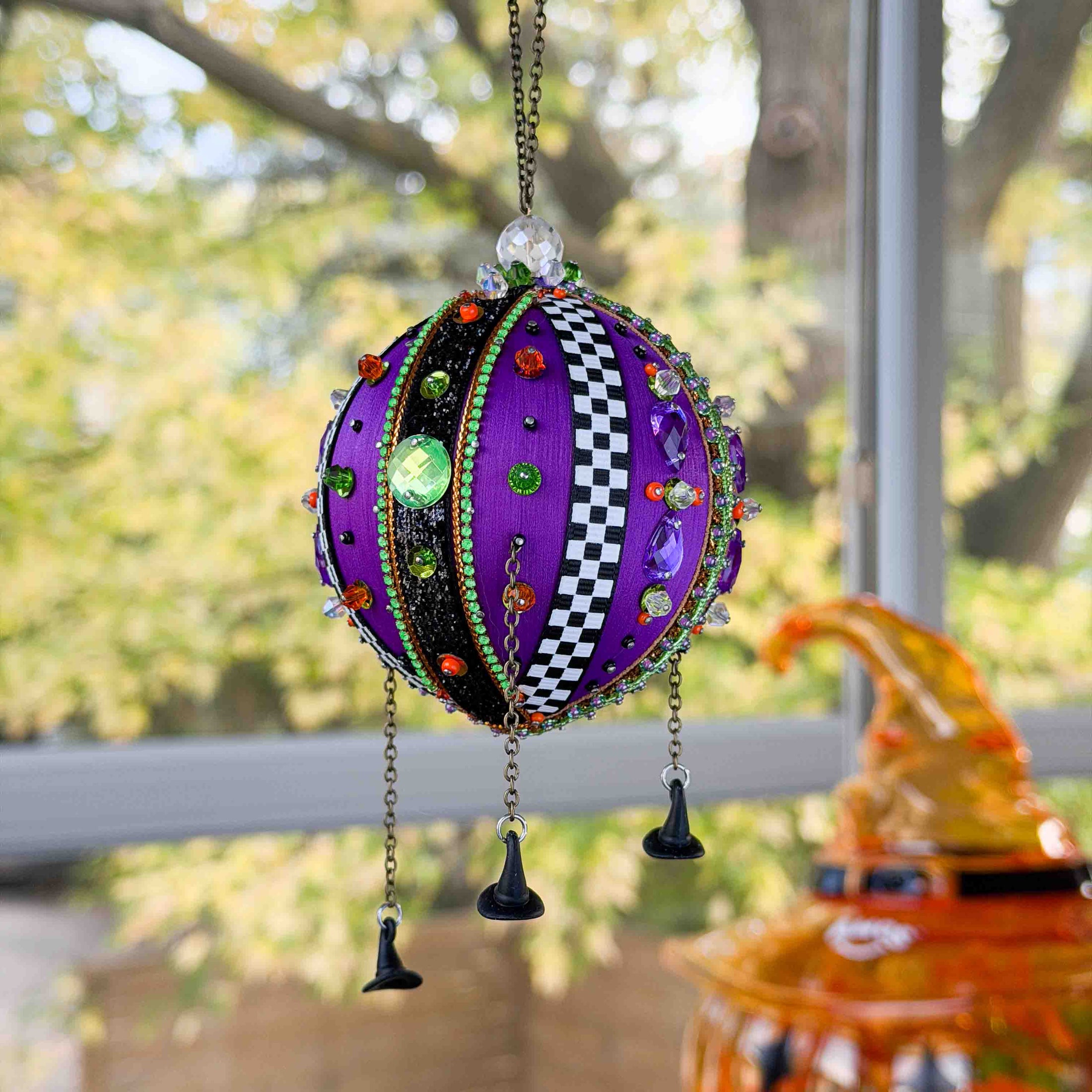 Decorative purple ornament with colorful embellishments hanging outdoors.
