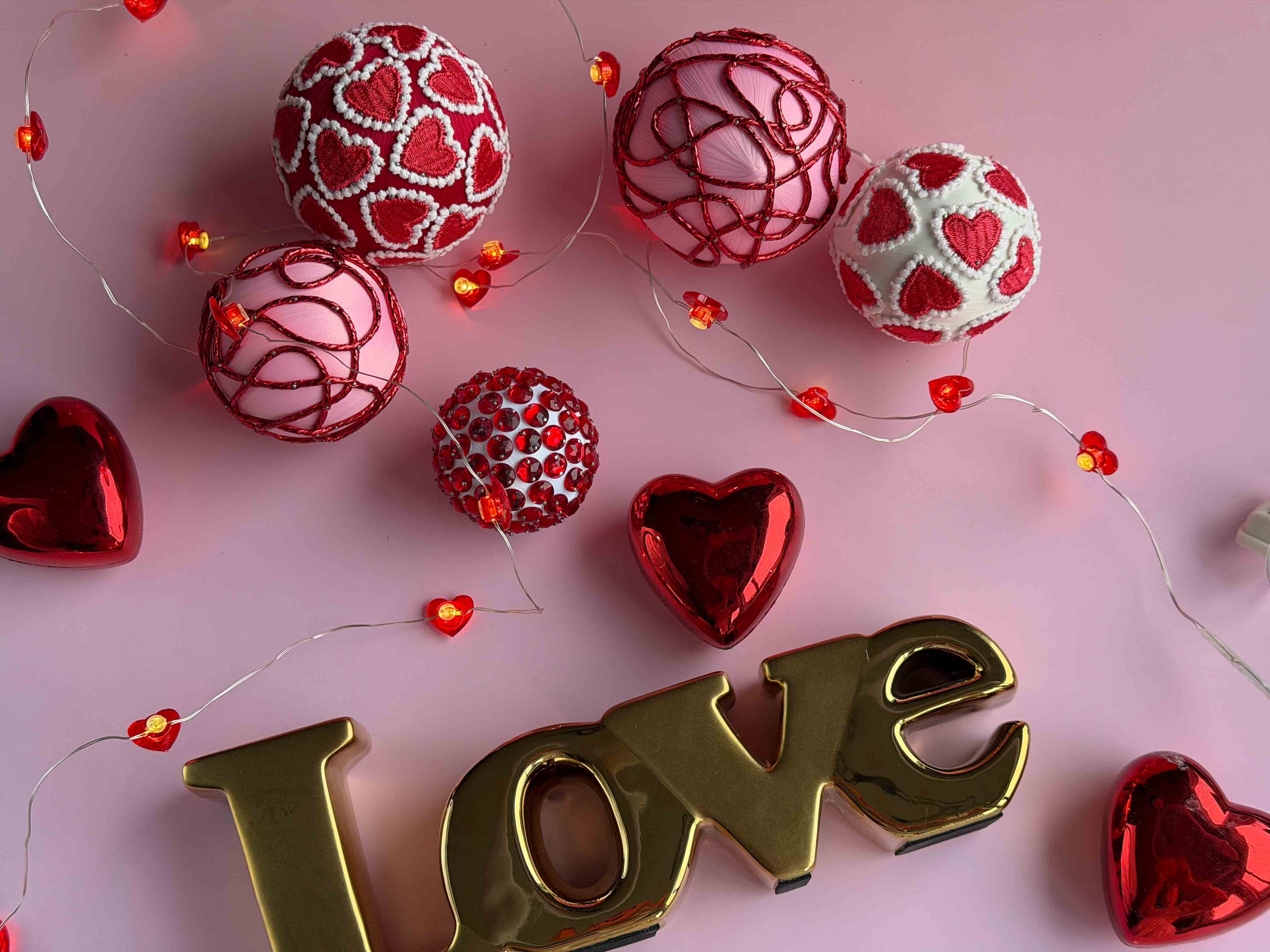Decorative arrangement with red and gold hearts and 'LOVE' letters on a pink background.