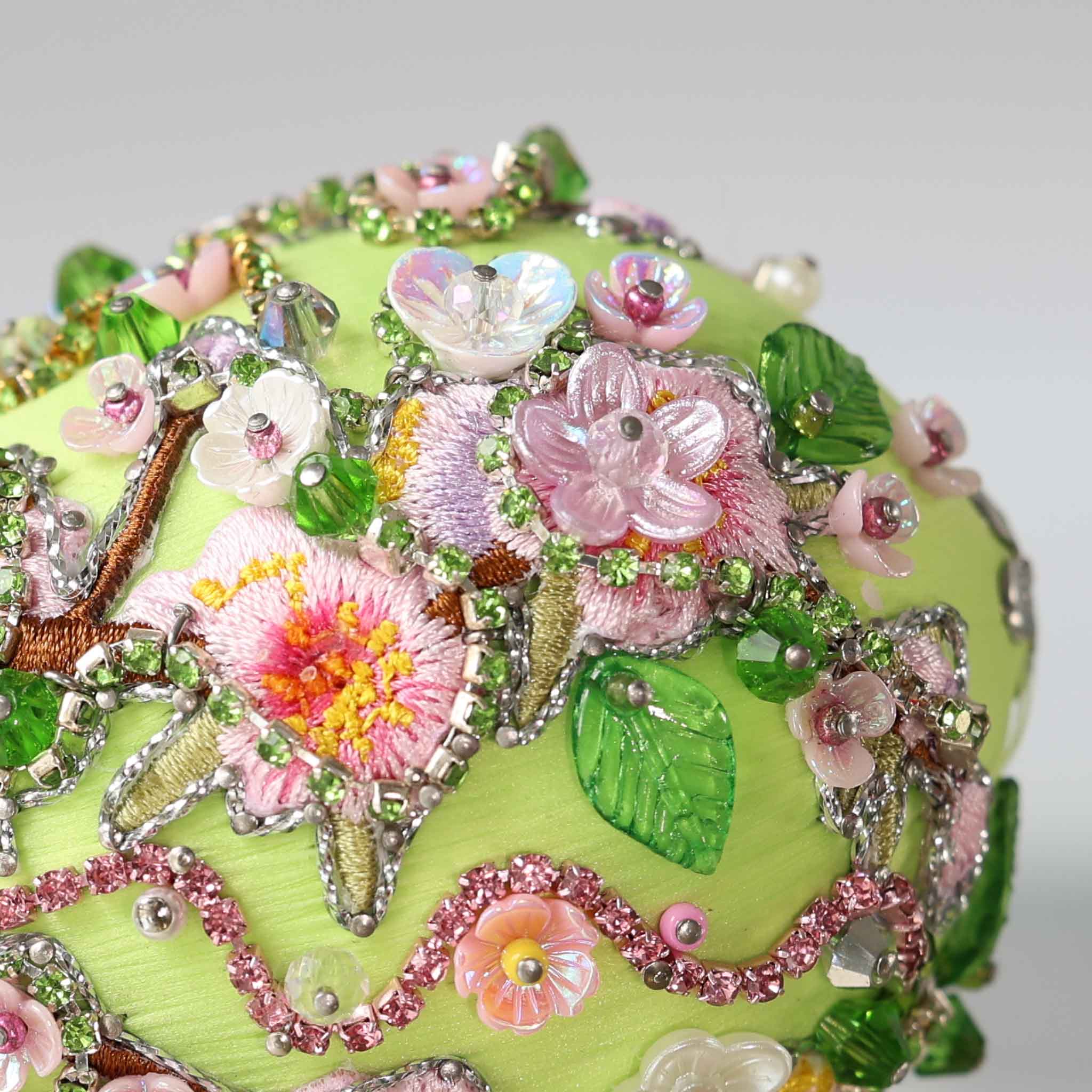 Close up of a handmade Easter Egg Push Pin Ornament embellished with tiny pink flowers and embroidered patches resembling Faberge style egg on a gray background by Whim5seasons.