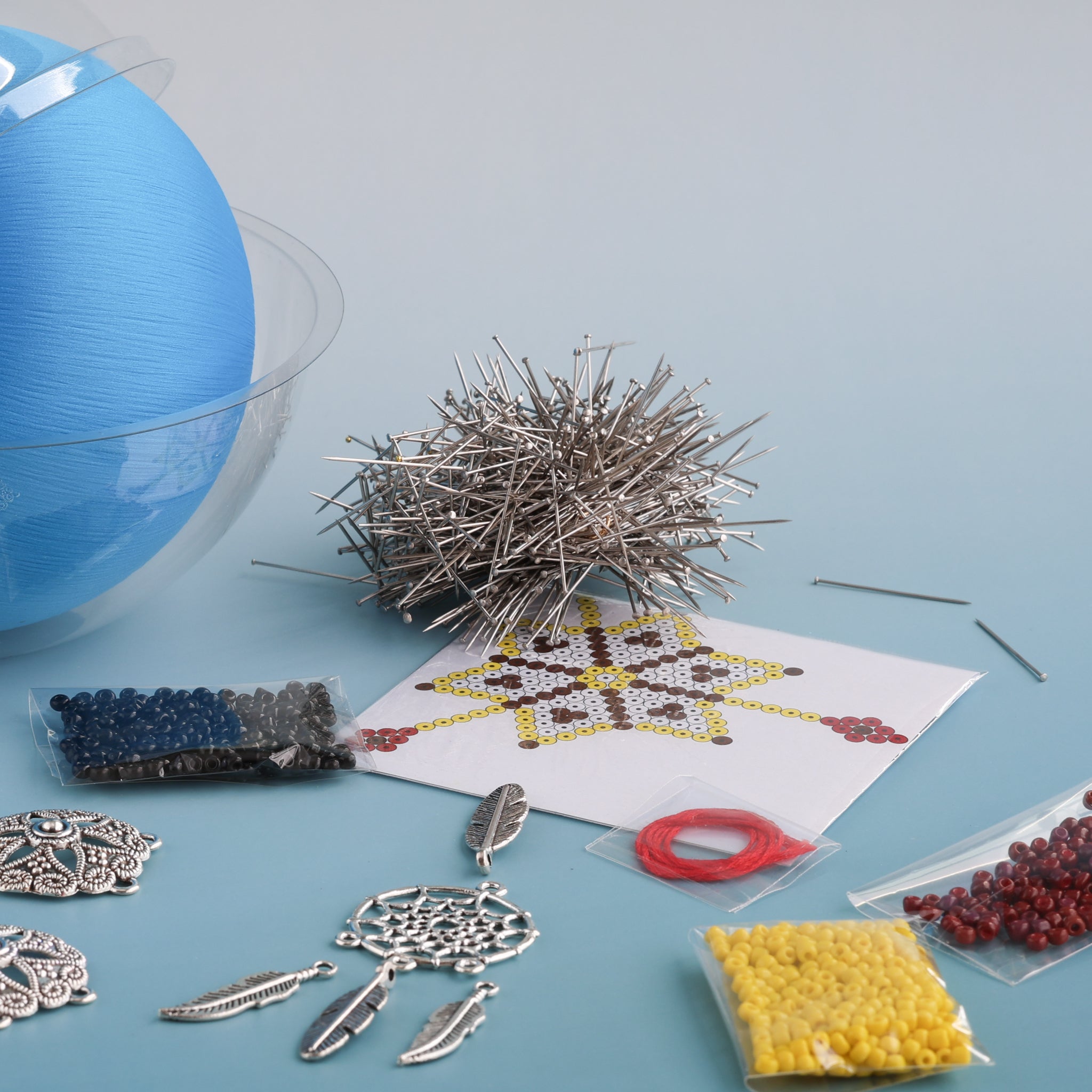 Satin ornament making supplies including beads, pins, and a silver dream catcher with feathers elements on a blue surface.  (Sky Blue) 