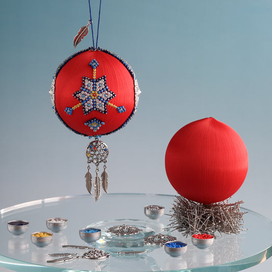Bright orange red 3" satin ball with a colorful star design and feather accents on a clear stand against a light blue background. (Crimson) 