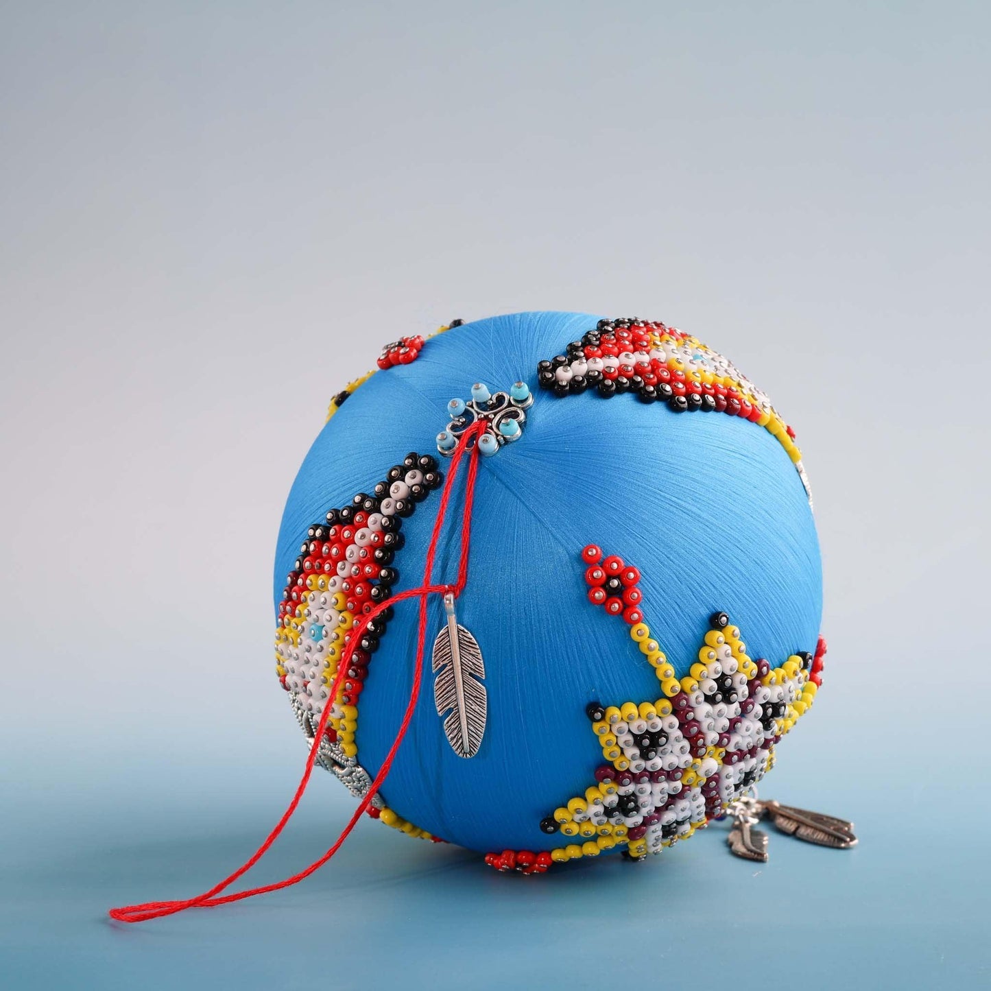 Decorative blue spherical object with bead patterns on a gray background.  (Sky Blue) 