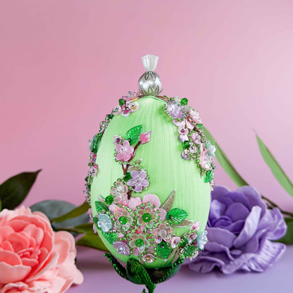 Decorative green egg with floral embellishments on a pink background with flowers.