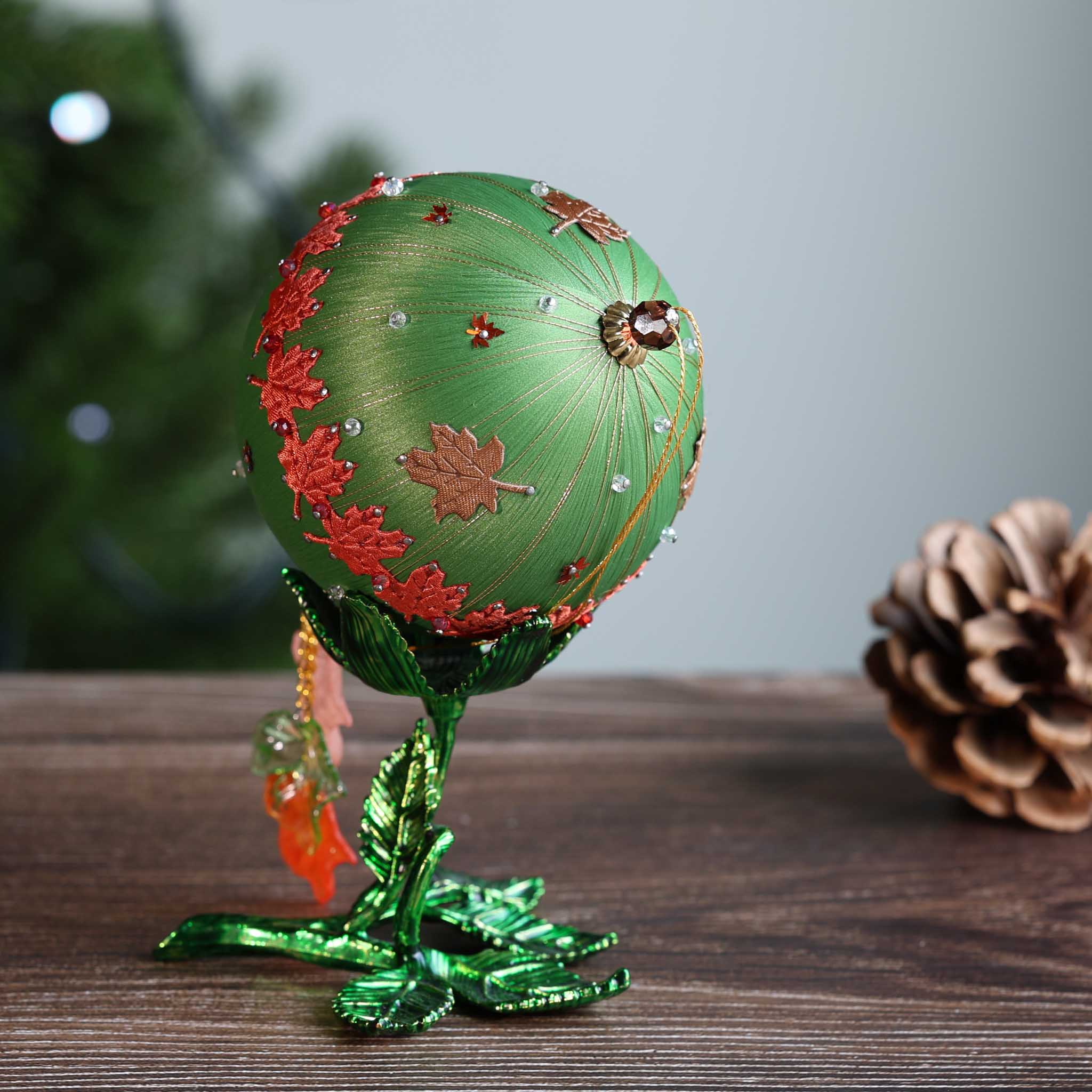 Christmas ball ornament wrapped in satin threads and embelished with red floral trim on a wooden surface. (Olive)