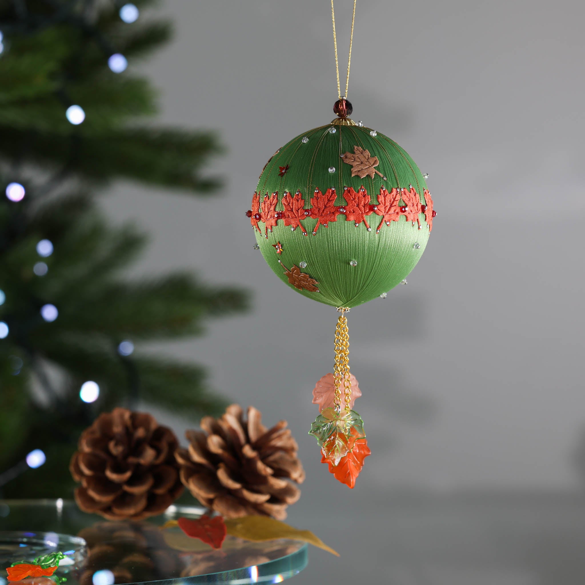 Olive green ornament hanging above pinecones in front of a Christmas tree. (Olive)