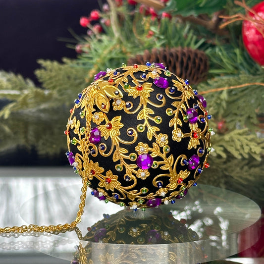 Quam Handmade Christmas Satin Ornament in Black with gold metal embellishments and purple rhinestones in front of evergreen branch. (Black)