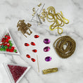 Load image into Gallery viewer, Materials to make Christmas Beaded Ornament by pinning glass rhinestones, gold braided trim, and crystal beads. to a satin ball. (Light Pink).

