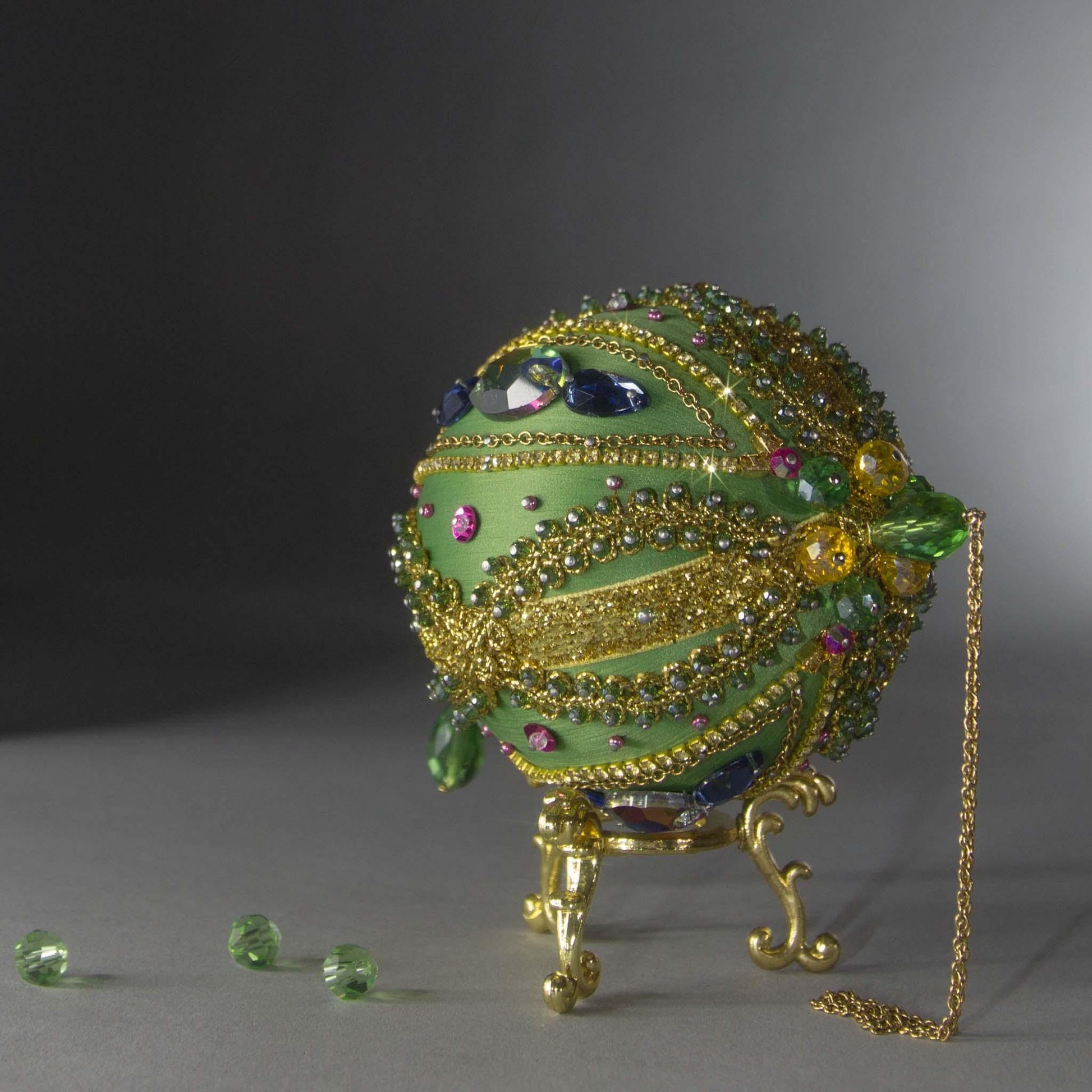 Christmas Beaded Ornament Ball embellished with large glass color-shifting rhinestones, gold braided trim, and crystal beads. Top detail. (Olive).