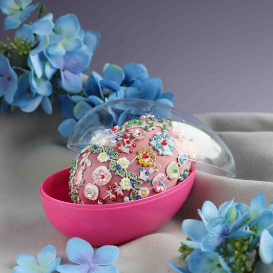 Decorative pink sphere with floral embellishments in a clear dome, surrounded by blue flowers on a soft background.  (Pale Violet Red)