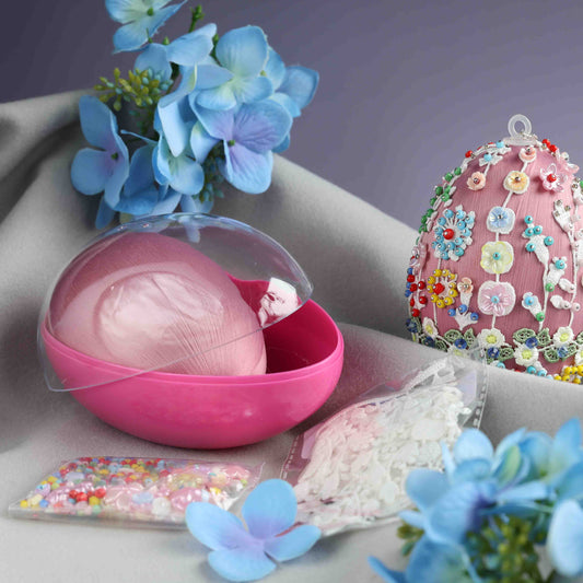 Pink decorative egg with a clear lid on a surface with flowers and a colorful embroidered egg. (Pale Violet Red)