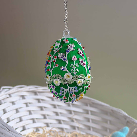 Decorative embroidered egg with floral patterns on a chain, placed on a woven surface. (Green)