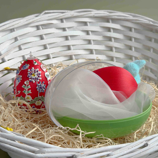 Decorative red egg with floral patterns in a white basket filled with straw and a green bowl. (Dark Red).