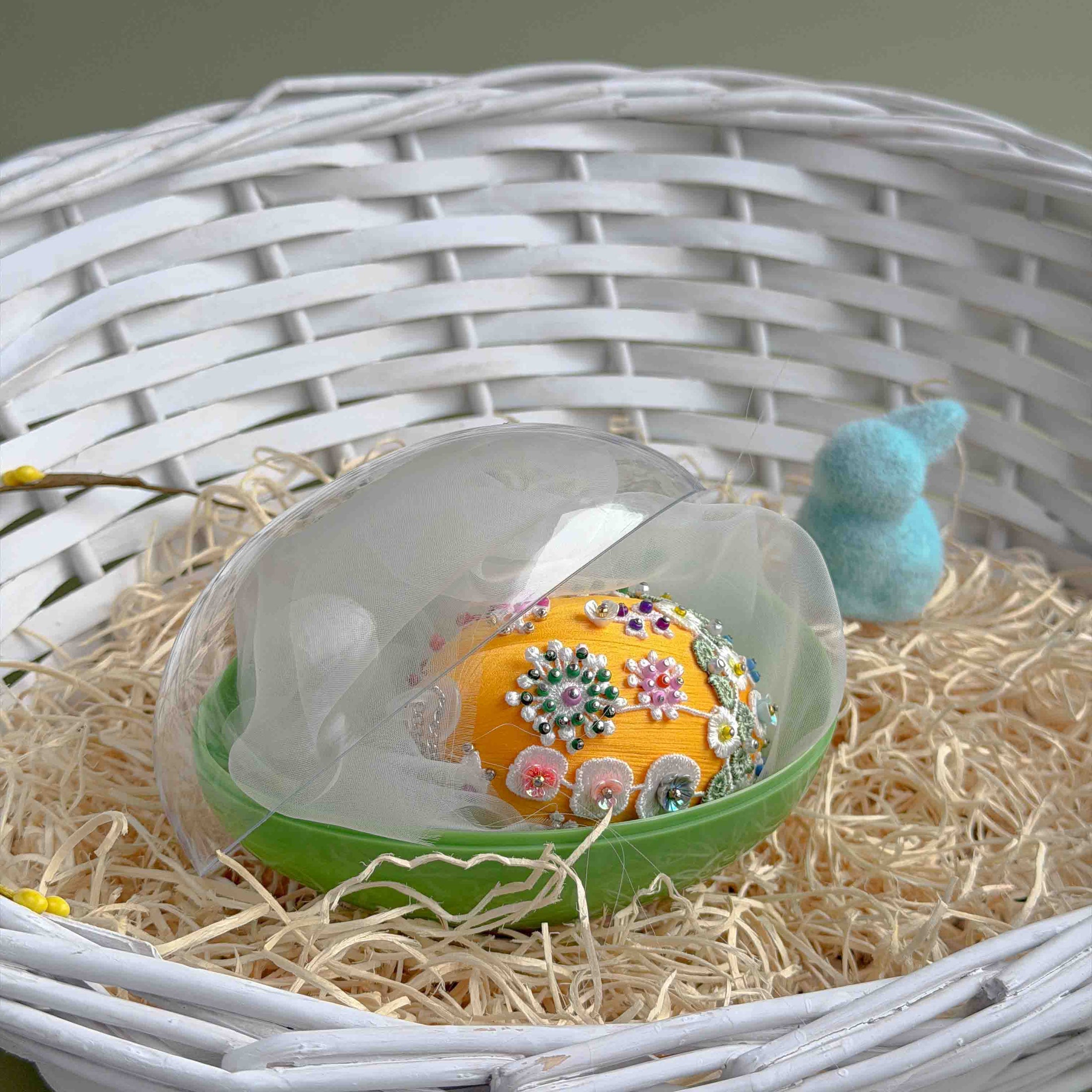 Handmade Easter egg with floral patterns in a clear storage container on a bed of straw. (Gold).
