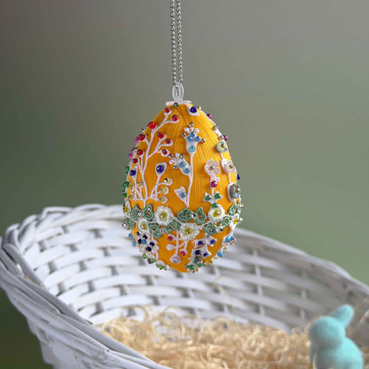 Easter egg with floral patterns and colorful beads hanging on a chain against a neutral background. (Gold).