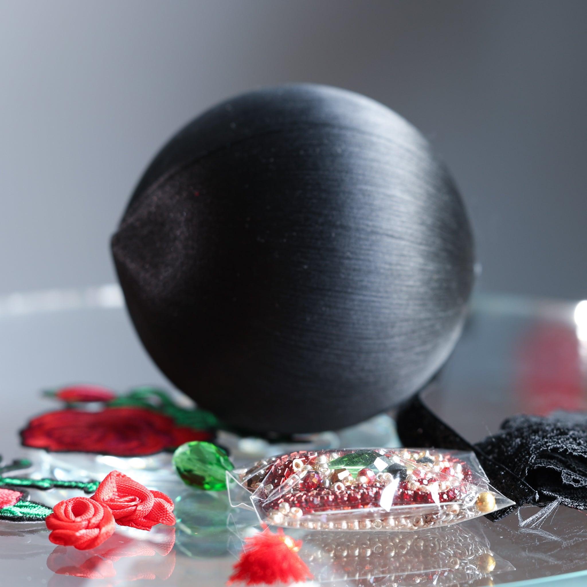 Black satin ball close-up on a reflective surface with decorative items around. (Black)