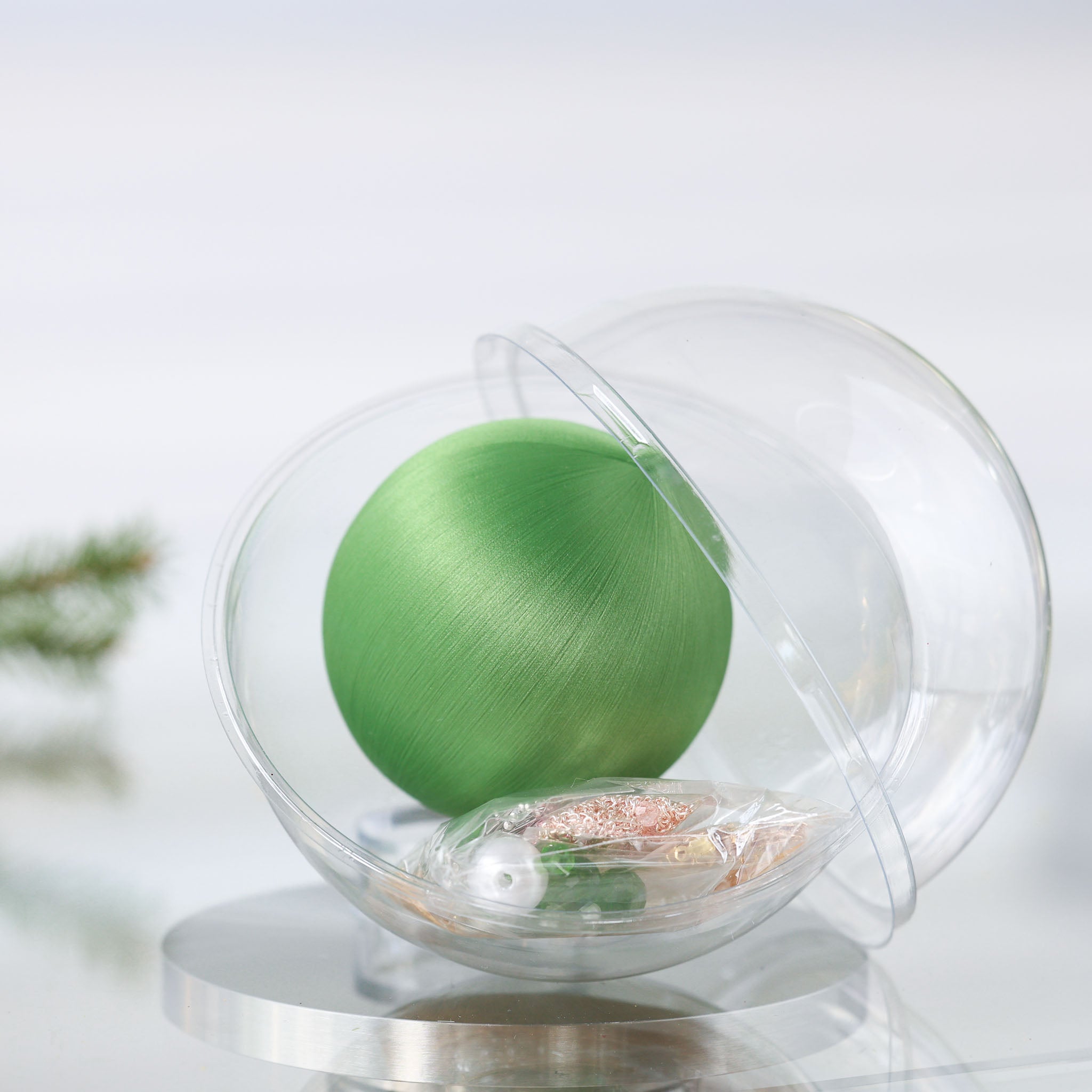 Satin Ornament Kit in a clear container with a green foam ball, and push pin kit materials in a small clear bag on a white background with holiday branch by Whim5seasons. (Olive)