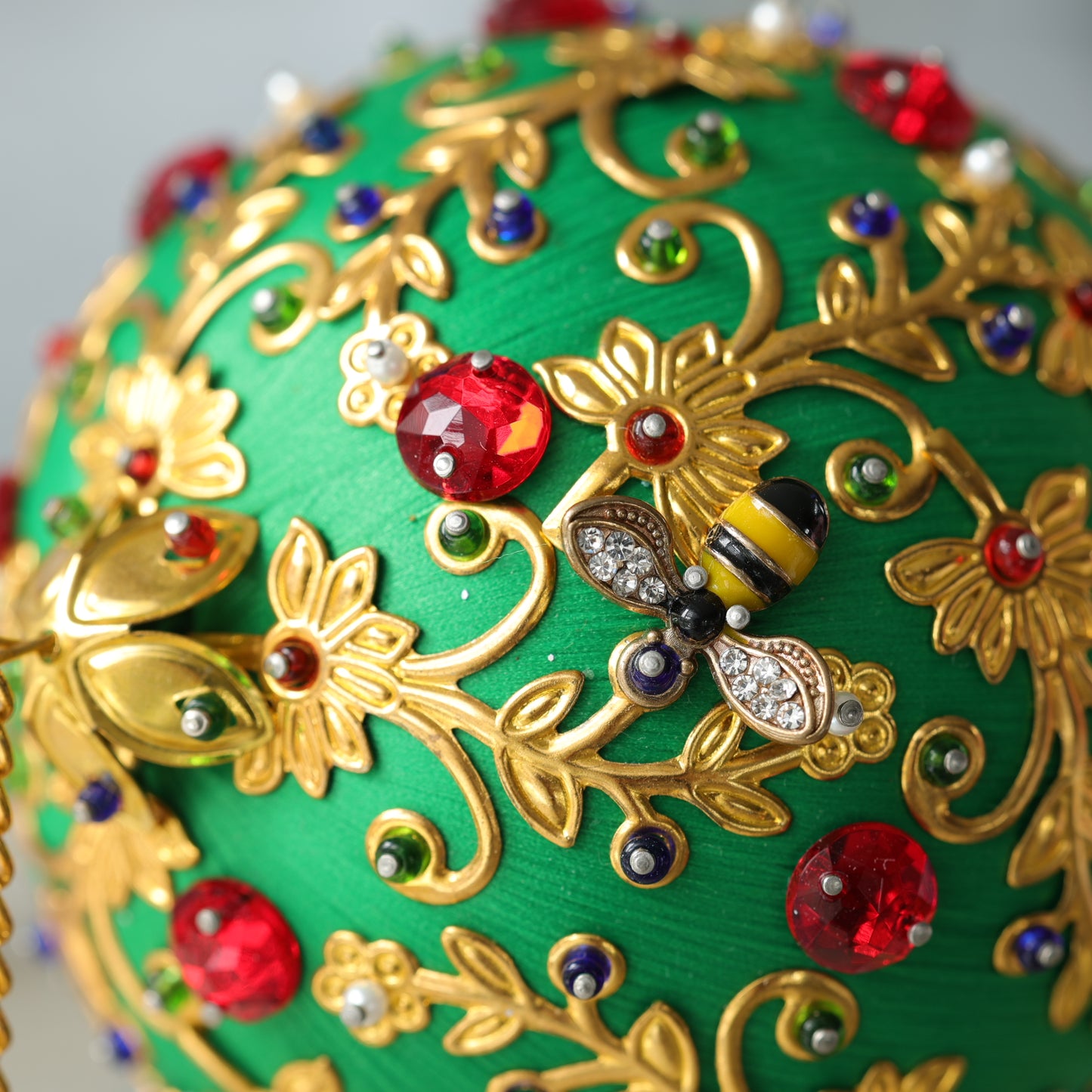 A close up of a handmade push pin ornament showing a small gold bee charm pinned to a satin ball with dressmaker pins by Whim5season.